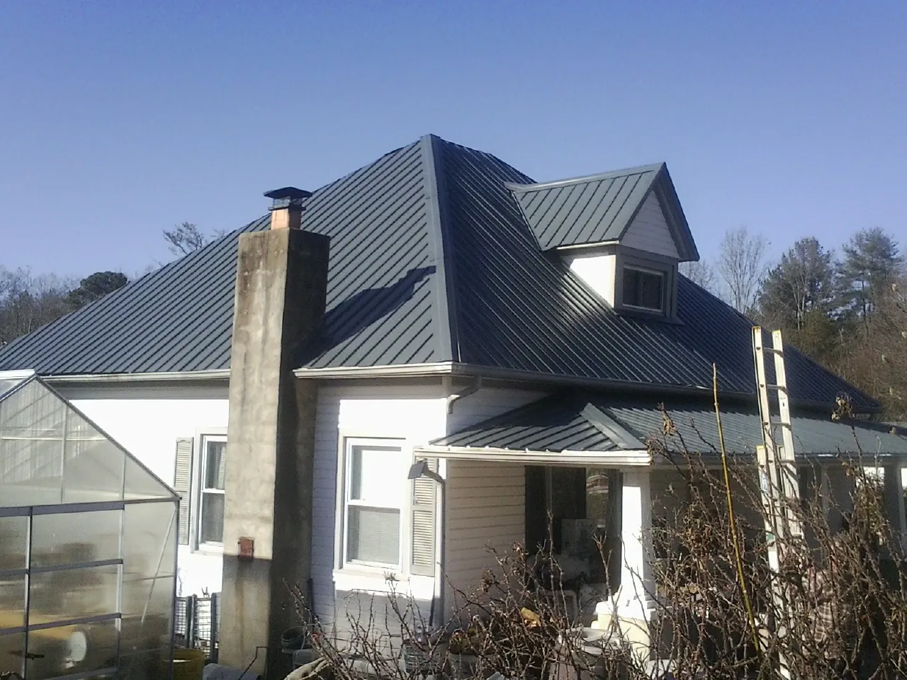 Dark blue standing seam metal roof on a white farmhouse with dormer — Slate & Tile Roof Repair by Roofing Brothers in Hanska