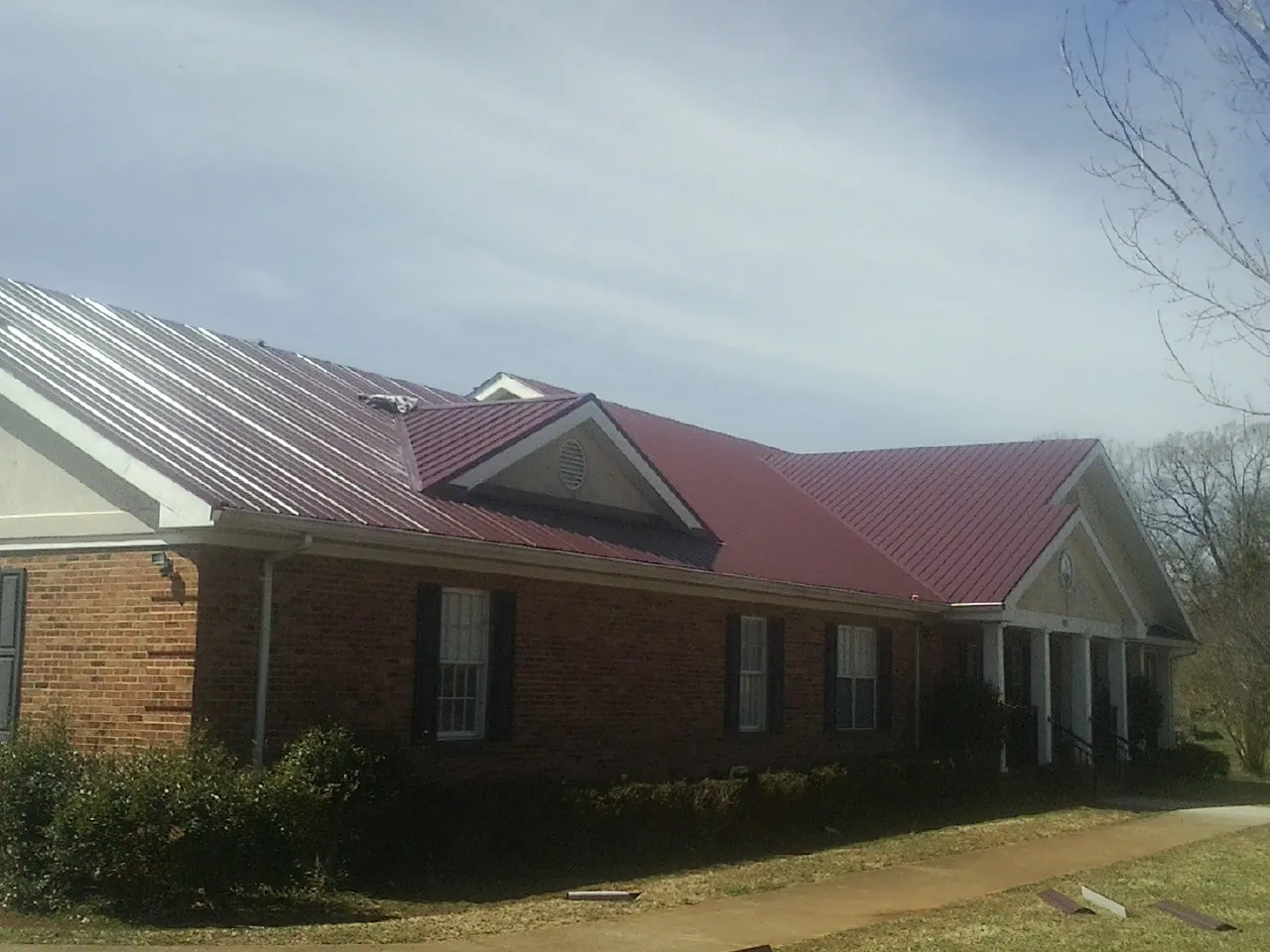 Red metal roof with gabled entries on a long brick building, from a Hail Damage Roof Repair job in Hanska