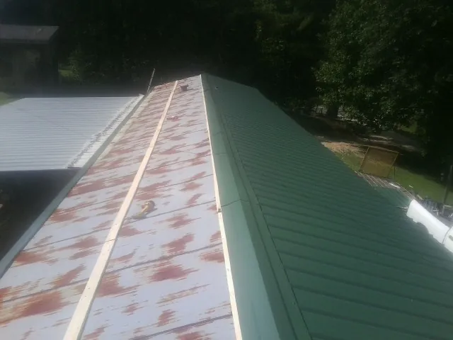 Old rusted panels beside newly installed green metal roofing — Wind Damage Roof Repair by Roofing Brothers in Hanska