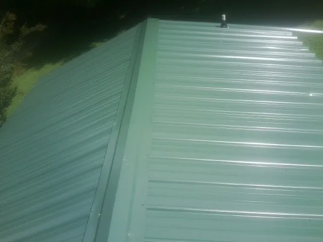 New green metal panels meeting at the ridge of a roof — Flat Roof Repair work by our crew in Hanska