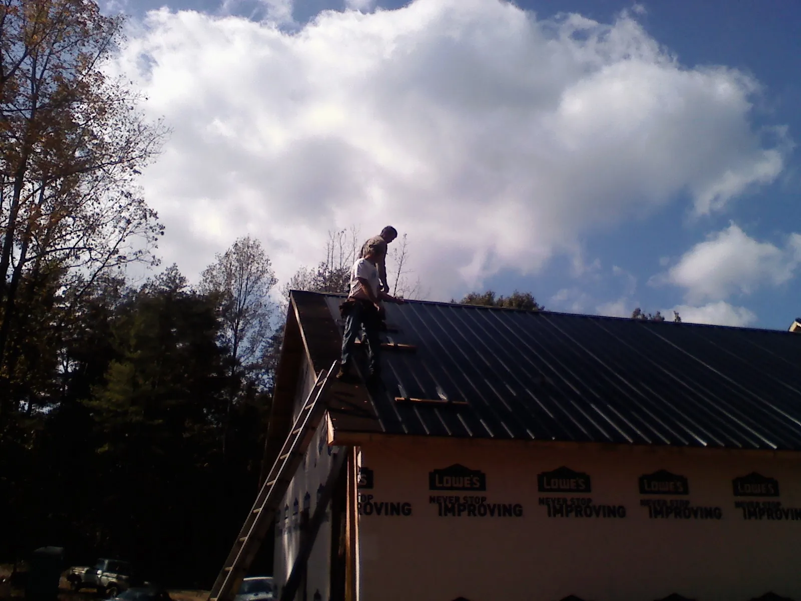 Roofer fastening dark metal panels high against a cloudy sky, from a Roof Inspection job in Hanska