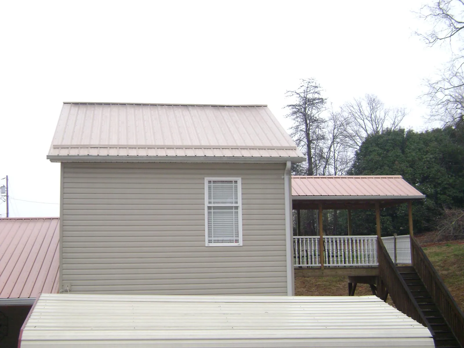 Tan metal roofs on a two story addition and attached porch, from a Roof Replacement job in Hanska
