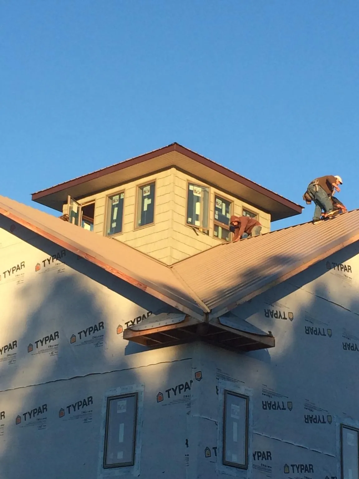 Roofers working around a rooftop cupola on a new metal roof at sunset — Roof Waterproofing in Hanska by Roofing Brothers